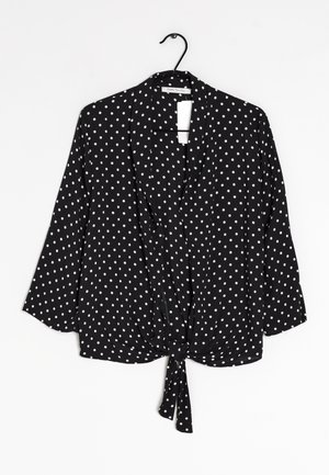 Blusa nera a pois bianchi con maniche a tre quarti, design con nodo frontale e tessuto leggero. Pois bianchi uniformemente distribuiti sul tessuto.