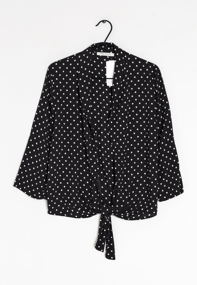 Svart blus med prickar, trekvartsärmar, knyt-fram design och lättviktig textil. Vita prickar jämnt fördelade över tyget.