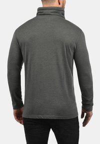 Donkergrijs shirt met lange mouwen en een hoge kraag, met een soepele textuur, gezien van achteren, gecombineerd met een zwarte jeans.