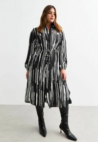 Un lungo vestito a righe bianche e nere realizzato in tessuto leggero, con colletto e cintura da annodare in vita. Abbinato a stivali neri fino al ginocchio.