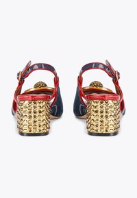 Denim slingback heels with red accents, gold studded block heels, and a decorative button at the back, featuring a smooth texture.