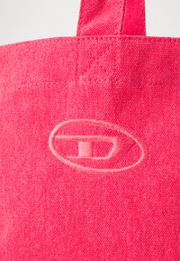 Sac fourre-tout en tissu rose avec un logo brodé dans une teinte rose plus claire, surface texturée et poignée renforcée.