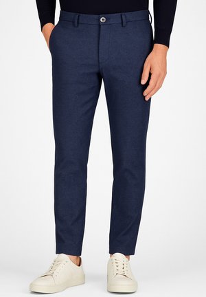 Pantalons navy avec une coupe ajustée, un tissu texturé, une fermeture à bouton à l'avant, des passants de ceinture, et associés à des baskets blanches.