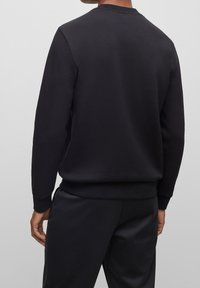 Černá mikina s dlouhými rukávy, žebrovaným výstřihem a manžetami. Měkká, textured tkanina s rovnou siluetou a minimalistickým stylem.