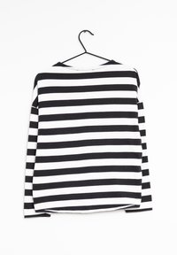 Dlouhá rukáv černobíle pruhovaná košile, se zaobleným výstřihem, měkkou tkaninou a uvolněným střihem se zakřiveným lemem. Visící na černém háčku.