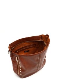 Braune Leder-Tote mit vertikalen Nieten auf der Vorderseite. Eine Innenzippertasche und glattes Futter sind sichtbar. Mit verdecktem Reißverschluss oben.