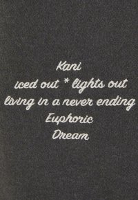 Black fabric with white embroidered text: "Kani iced out * lights out living in a never ending Euphoric Dream." Soft, textured surface.