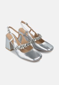 Scarpe slingback con tacco argentato, punta squadrata, cinturino decorato con cristalli trasparenti e design con tacco a blocco. Finitura metallica liscia.
