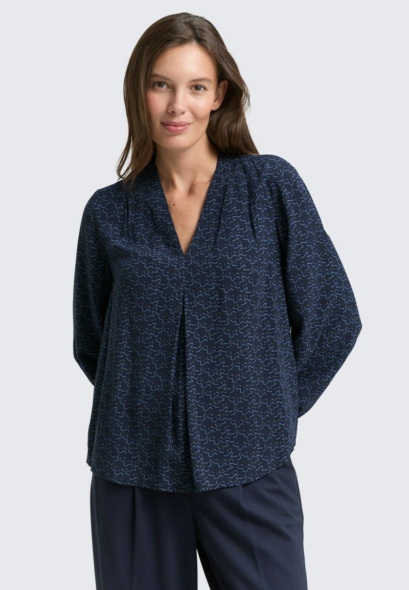 Navy blouse with a V-neck and long sleeves, featuring a subtle white wavy line pattern. Soft fabric with a relaxed fit and tucked pleat detail.