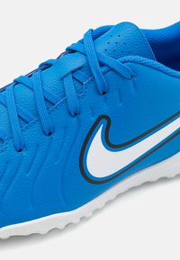 Blue synthetic soccer shoe with textured upper, contrasting white logo, layered design, and blue laces. Rubber sole with traction pattern.
