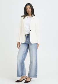 Blazer blanc ajusté sur une chemise blanche, associé à un jean large bleu clair et des escarpins marron à bout pointu. Textures lisses, sans motifs.