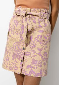 Jupe à motifs floraux en beige clair avec des accents violets et jaunes, dotée d'une taille à nouer, de boutons et de poches latérales.