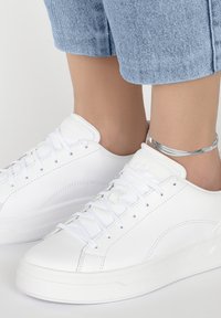 Sneakers bianchi in pelle con punta rotonda, lacci piatti bianchi, dettagli di cucitura sottili e suola texturizzata, abbinati a denim azzurro chiaro.