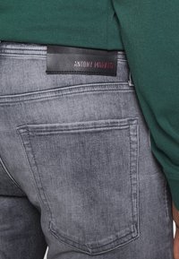 Jeans de mezclilla gris con un corte slim, que cuentan con un bolsillo trasero y una etiqueta negra con "ANTONY MORATO" en texto rojo. Tejido suave y texturado.
