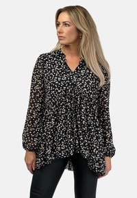 Czarna bluzka z szyfonu z kwiatowym wzorem w białym i kremowym kolorze, marszczonym gorsetem, długimi rękawami i dekoltem w serek. Luźny krój z płynną sylwetką.