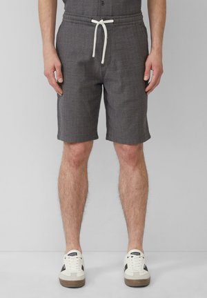 Grau gemusterte Shorts mit einem elastischen Bund und weißem Kordelzug, mit flachem Vorderteil und seitlichen Taschen, kombiniert mit weißen Sneakers.