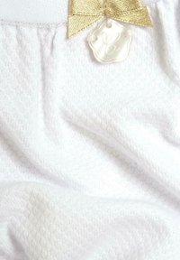 Tessuto bianco morbido con un motivo testurizzato; presenta un fiocco dorato e un'etichetta rotonda color crema con un design in rilievo.