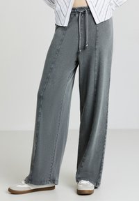 Pantalons légers à jambes larges en denim gris. Comprend une taille élastique avec cordon de serrage et des coutures contrastées. Associés à des baskets décontractées.