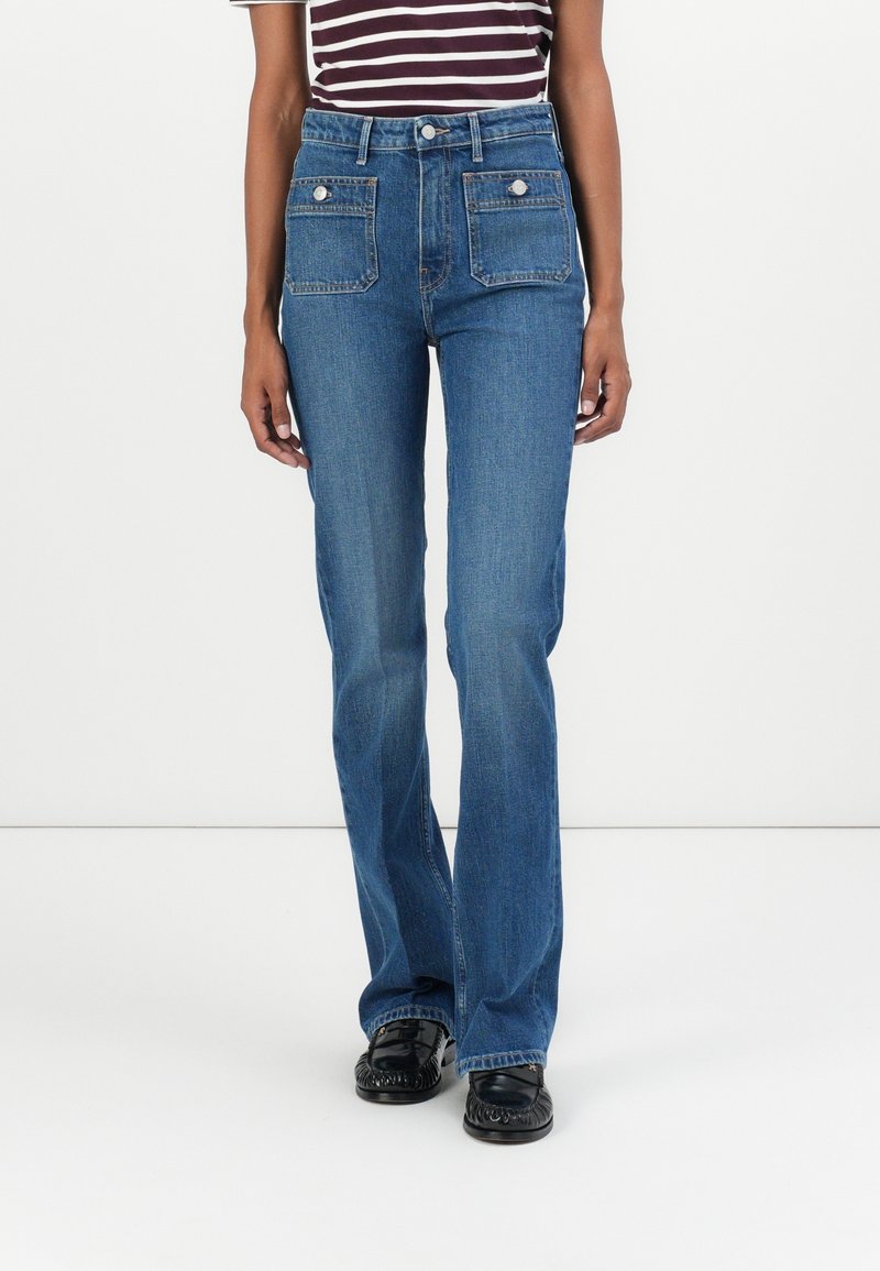 Femme portant un jean bleu taille haute à jambes droites avec de grandes poches à rabat sur le devant et des mocassins noirs, associé à un haut rayé à manches courtes.
