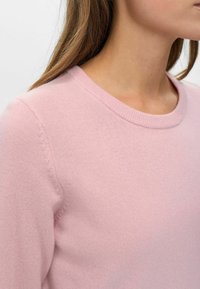 Lichtroze trui met een ronde hals, gemaakt van zacht materiaal. Heeft een geribbelde kraag en een gladde textuur overal.