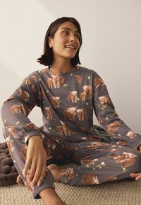 Graues Pyjama-Set mit langem Arm, das ein wiederholtes Muster aus braunen Tieren und grünen Akzenten zeigt. Weicher Stoff mit elastischen Bündchen.