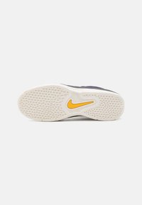 Nike cipőtalp, textúrált fehér gumiból, sárga akcentus logóval, fekete alappal és lila részletezéssel.