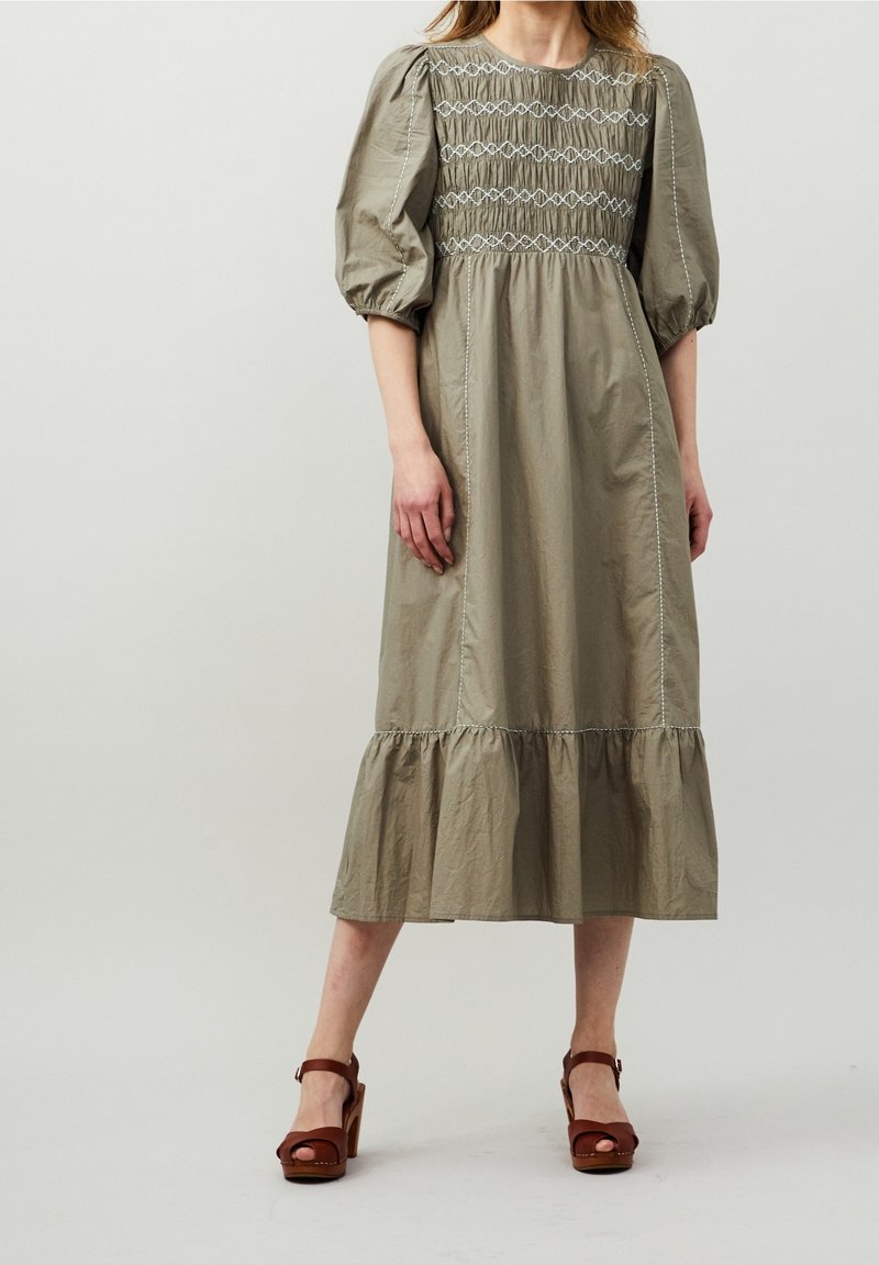 Jasnozielona sukienka do kolan z rękawami do łokci, marszczonym gorsetem i falbaniastym dołem. Uzupełniona brązowymi sandałami na drewnianym obcasie.