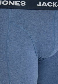 Gros plan sur un boxer bleu pour hommes avec une ceinture noire marquée "JACK & JONES" et des coutures visibles sur le tissu.
