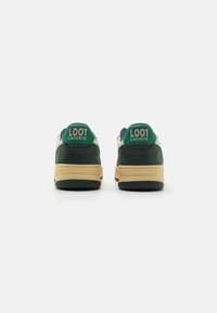 Green suede sneakers with white leather accents, featuring "L001" and "LACOSTE" in pink on the heels and tan rubber soles.