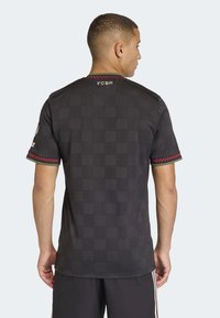 Black short-sleeve jersey with a textured pattern, featuring a red and green striped trim on sleeves and “FCBM” lettering at the neck.