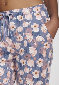 Leichte Stoffhose mit Blumenmuster, die sanfte rosa und weiße Blumen auf blauem Hintergrund zeigt, mit einem elastischen Bund und Seitentaschen.