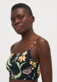 Květinový crop top s tenkými ramínky, s oranžovými a žlutými květinami na námořnickém pozadí a hladkou, elastickou texturou materiálu.