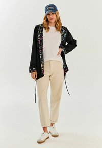 Čierna ľahká bunda s kvetinovou podšívkou, doplnená bielym tričkom a béžovými zúženými nohavicami. Model má na hlave džínovú čiapku a športové tenisky.