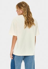 Krémové oversized tričko s krátkými rukávy, kulatým výstřihem a hladkou bavlněnou texturou, spárované s modrými džíny.