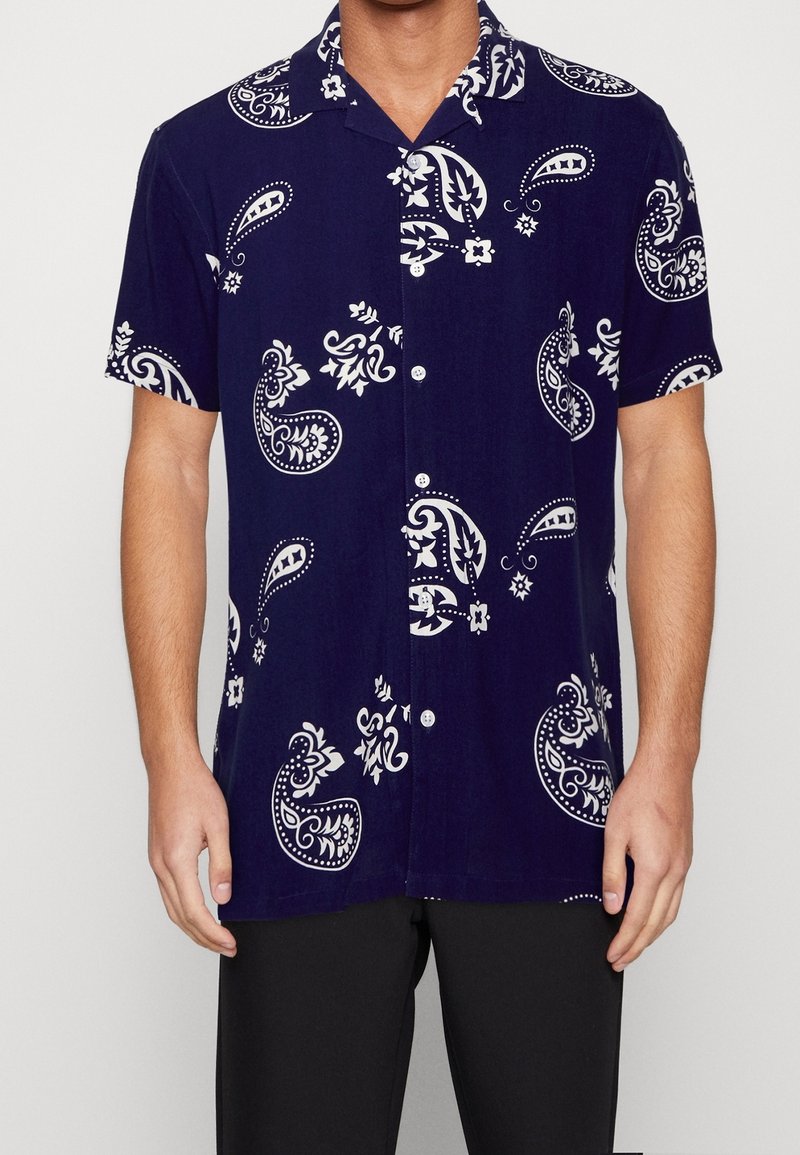 Košile s krátkým rukávem v námořnicky modré látce s bílými paisley a květinovými vzory, se zapínáním na knoflíky vpředu a volným střihem.