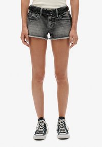 Denim shorts in vervaagd zwart met gefringeerde zoom, voorzien van voorzakken en een gevlochten riem. Gemaakt in combinatie met zwarte high-top sneakers.