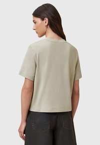 T-shirt a maniche corte di colore verde chiaro con scollatura rotonda, texture liscia e vestibilità rilassata, abbinato a pantaloni scuri e cuciture minime.