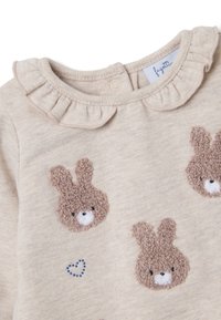 Beige pullover top met een gerimpelde halslijn, drie pluizige konijn-applicaties en een klein blauw hartje in stiksel.