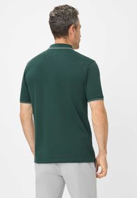 Grünes Polohemd mit kurzen Ärmeln, kontrastierender weißer Rand am Kragen und an den Ärmelabschlüssen, aus glattem, dehnbarem Stoff.