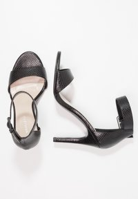 Sandales à talons hauts noires avec une texture en cuir de serpent, un bout ouvert, une large bride avant et une bride de cheville avec un détail de boucle.