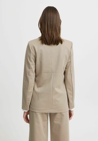 Beige blazer med en strukturerad design, långa ärmar och rak rygg. Slät textur med minimal sömnad och ingen synlig hårdvara.