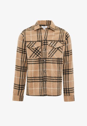 Een tan geruite flanellen shirt met zwart-witte lijnen. Heeft twee borstzakken, knoopsluiting aan de voorkant en een afgeronde onderkant. De stof heeft een zachte textuur.