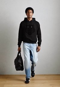 Felpa nera con design di leone, jeans azzurri chiari, sneakers nere e una borsa nera. La texture è liscia con una vestibilità casual.