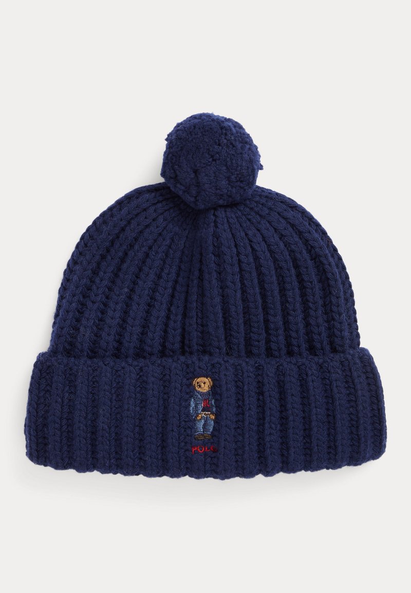Granatowa prążkowana czapka dzianinowa z pomponem na górze oraz małym haftowanym misiem w kurtce ponad mankietem.