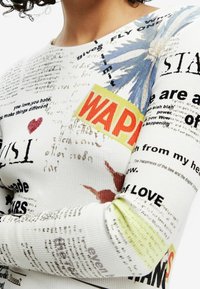 Ribbed pitkähihaisena paitana, jossa on valkoinen pohja ja monivärisiä tekstejä, grafiikoita ja kuvioita, mukaan lukien sininen kukkakuosi ja voimakkaat korostukset.