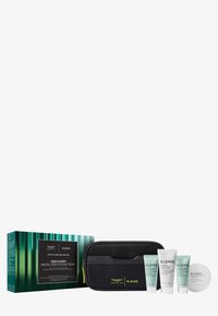 Collezione di prodotti per la pelle in una custodia nera con zip. Include tre contenitori a tubetto e un barattolo rotondo, tutti con etichette verde chiaro e bianche.