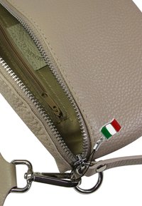 Beige leren handtas met een textuurafwerking, voorzien van een zilveren rits en een klein Italiaans vlaggetje als bedeltje aan de ritshendel.