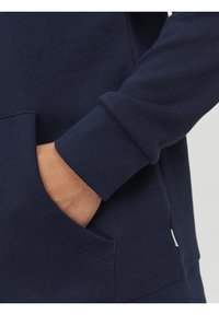 Sudadera azul marino con bolsillo tipo canguro, puños de canalé y textura de tela suave. El diseño presenta un estilo minimalista sin patrones ni gráficos.