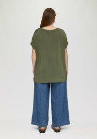 Luźna oliwkowa koszulka z krótkim rękawem, w połączeniu z szerokimi niebieskimi dżinsami. Gładka tekstura, swobodna sylwetka.