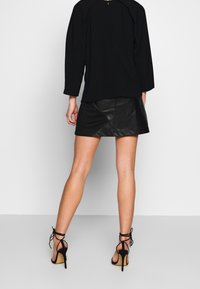 Svart långärmad topp, svart läder minikjol med diagonala sömmar och svarta strappy högklackade skor med öppen tå. Släta texturer genomgående.